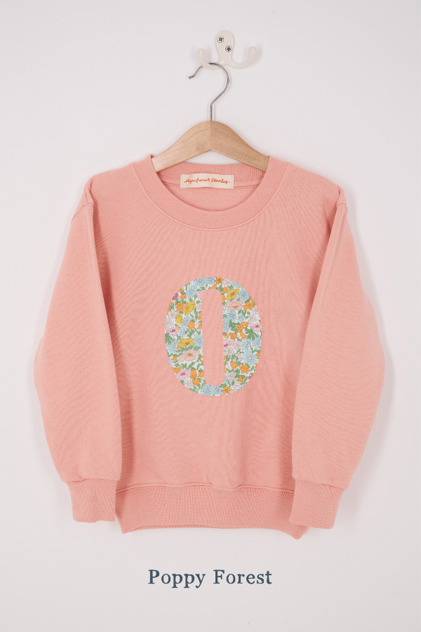 A pink personalised sweatshirt with an initial sewn on to the front. The initial is made from floral poppy forest liberty print