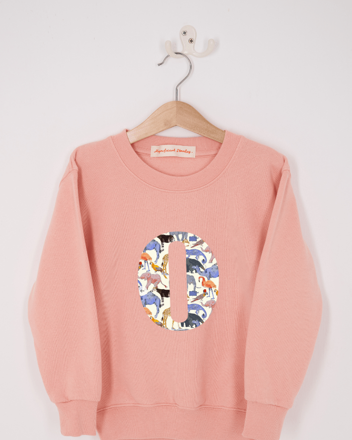A pink personalised sweatshirt with an initial sewn on to the front. The initial is made from Queue for the Zoo liberty print