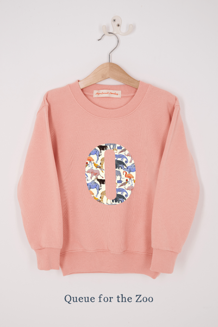 A pink personalised sweatshirt with an initial sewn on to the front. The initial is made from Queue for the Zoo liberty print
