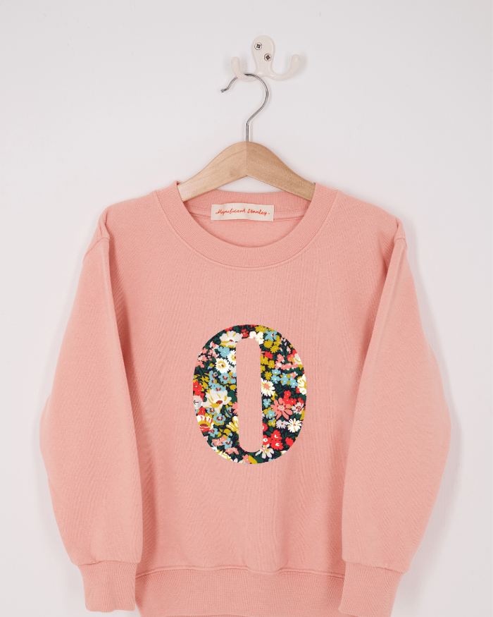 A pink personalised sweatshirt with an initial sewn on to the front. The initial is made from Thorpe floral liberty print.