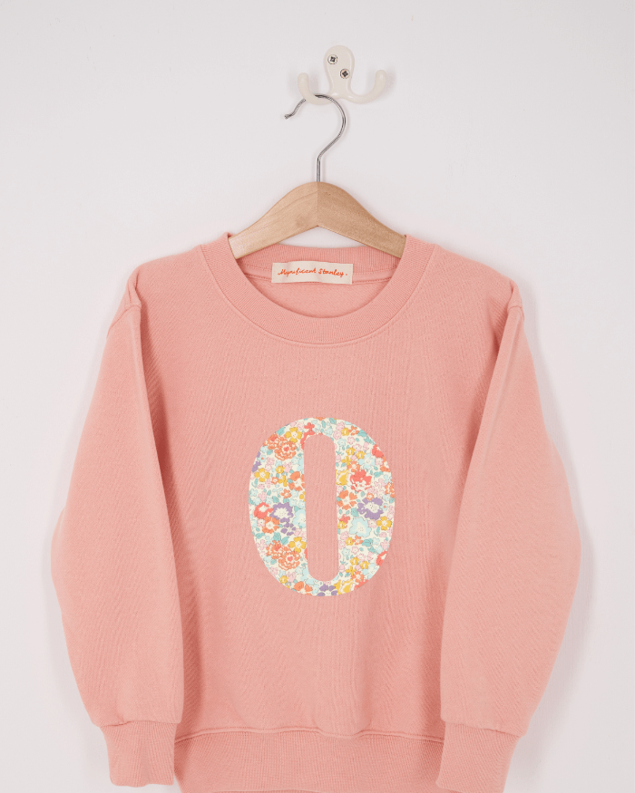 A pink personalised sweatshirt with an initial sewn on to the front. The initial is made from Michelle floral liberty print