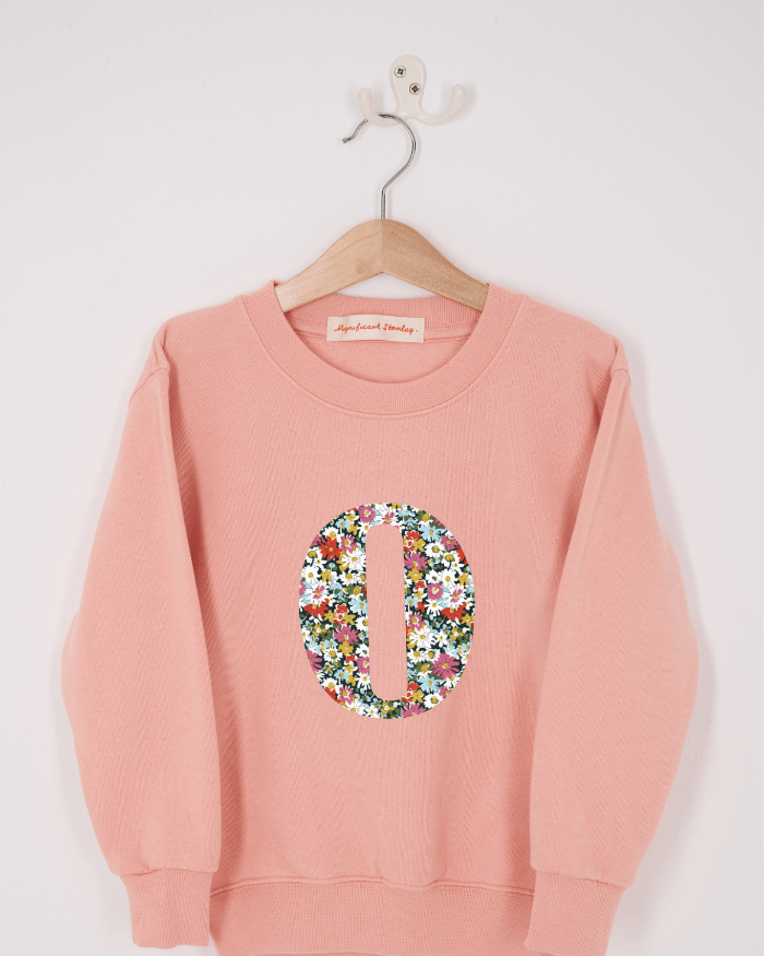 A pink personalised sweatshirt with an initial sewn on to the front. The initial is made from Libby floral liberty print