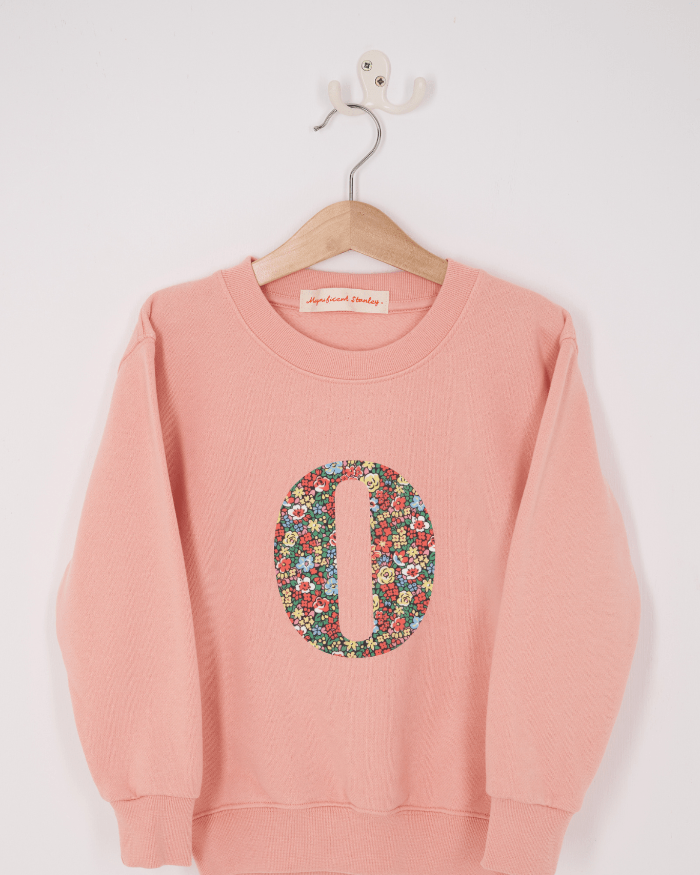 A pink personalised sweatshirt with an initial sewn on to the front. The initial is made from floral Emma Louise liberty print