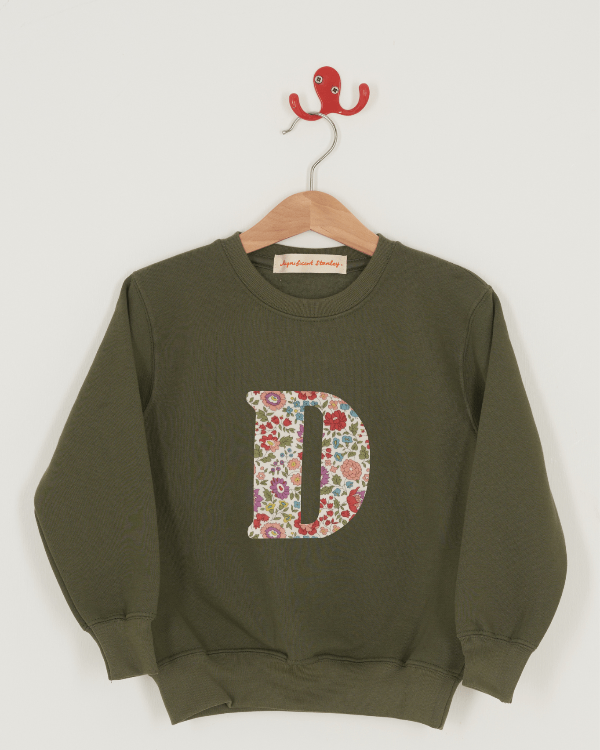 A khaki sweatshirt with an initial on the front. The initial is made from D'Anjo floral Liberty print.