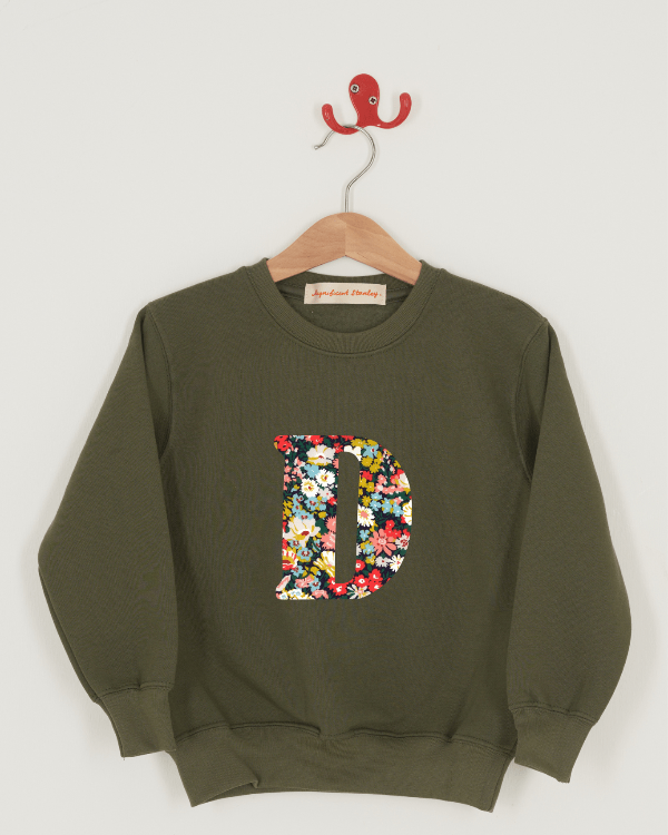 A khaki sweatshirt with an initial on the front. The initial is made from Thorpe floral Liberty print.