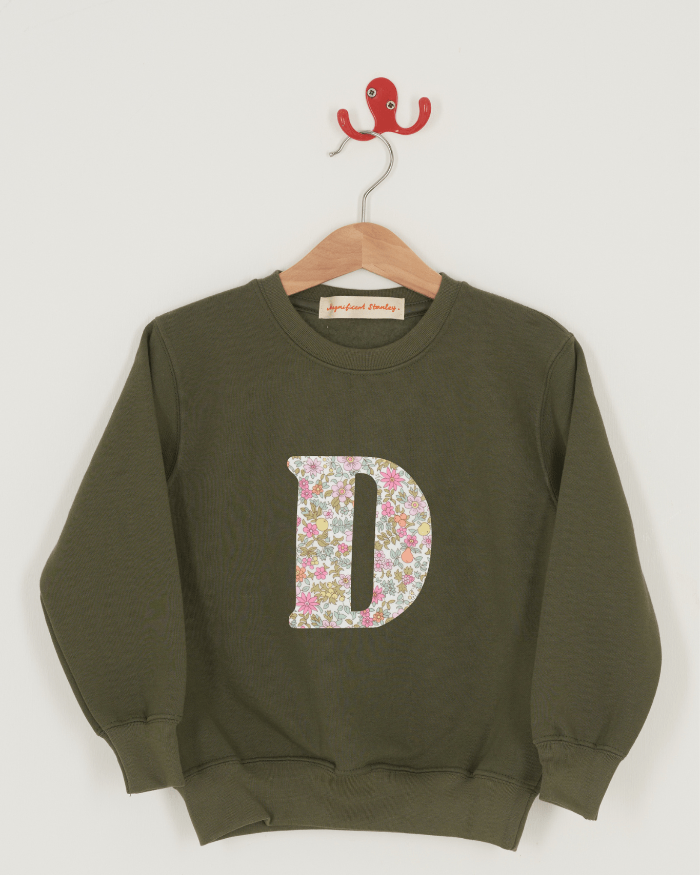 A khaki sweatshirt with an initial on the front. The initial is made from pink floral Liberty print.