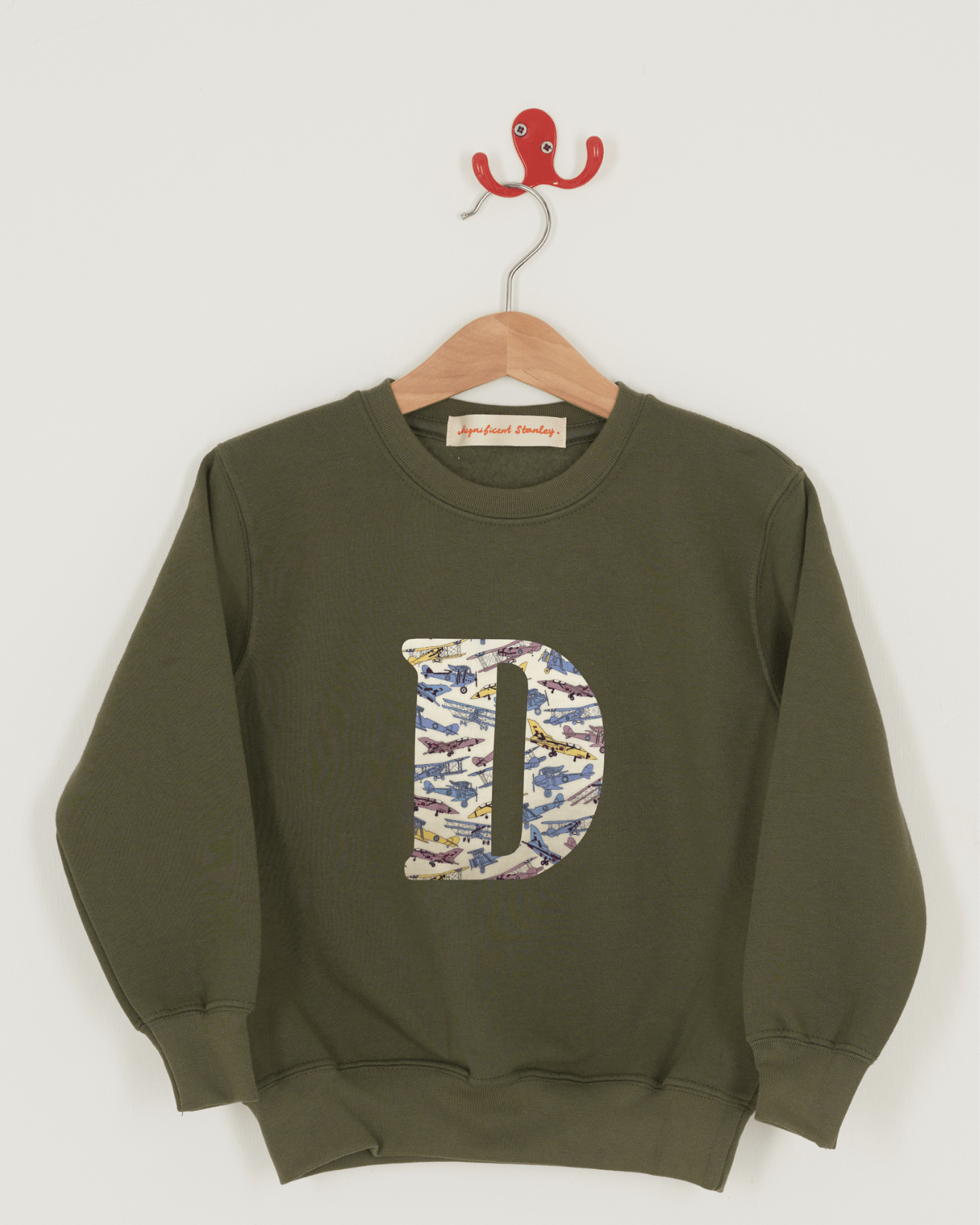 A khaki sweatshirt with an initial on the front. The initial is made from Liberty print featuring vintage jet planes.