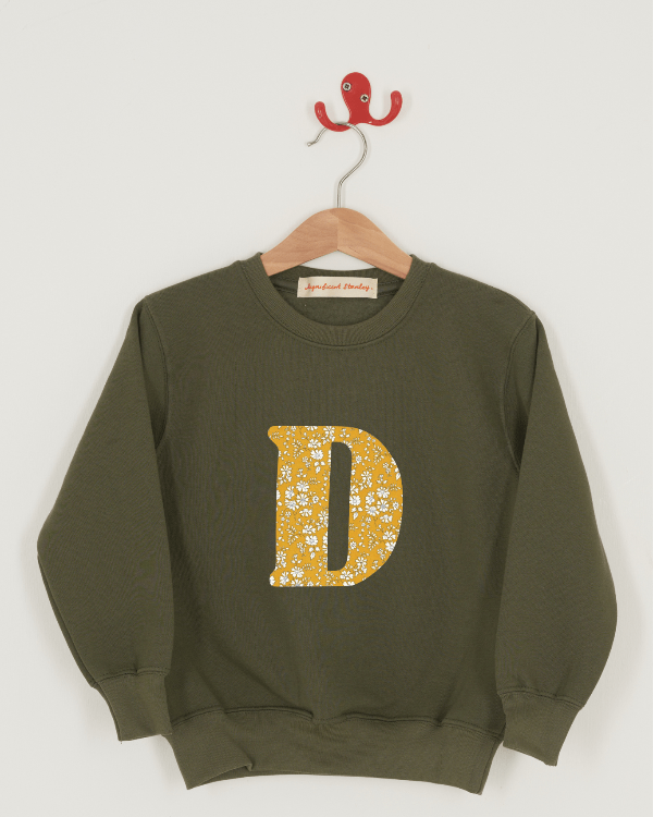 A khaki sweatshirt with an initial on the front. The initial is made from Capel floral Liberty print.