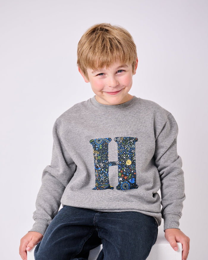 a 7 year old  boy wearing a personalised Magnificent Stanley Grey kids Sweatshirt with his initial on in Adelajda in Space liberty print.