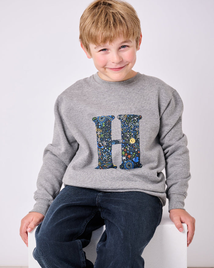 a 7 year old boy wearing a personalised Magnificent Stanley Grey kids Sweatshirt with his initial on in Adelajda in Space liberty print.