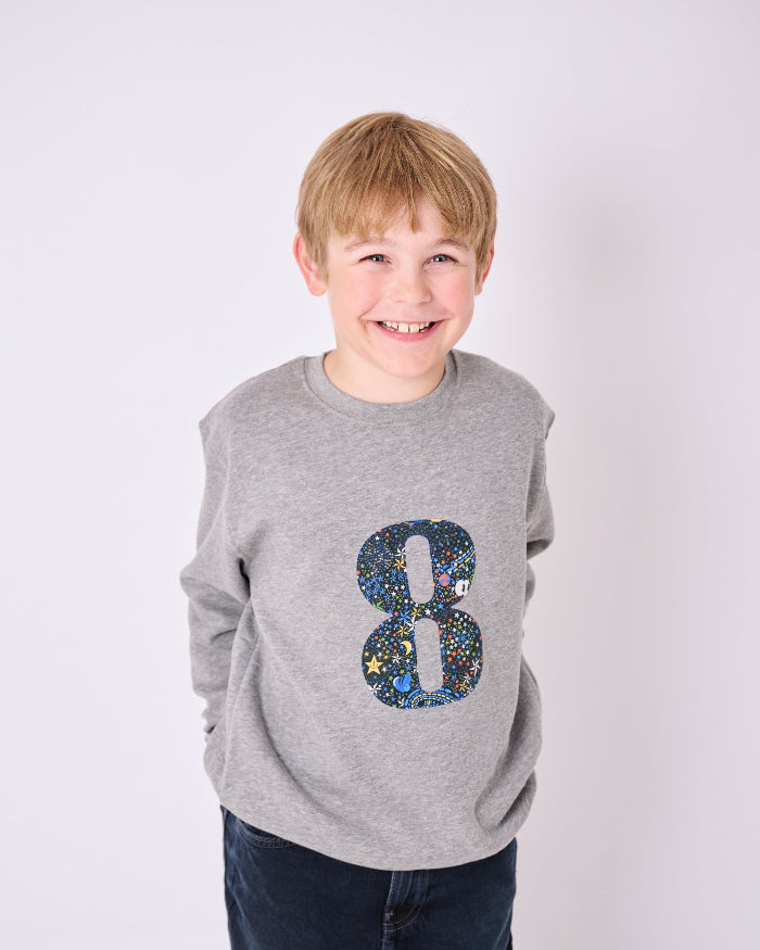 a 7 year old  boy wearing a personalised Magnificent Stanley Grey kids Sweatshirt with his initial on in Adelajda in Space liberty print.