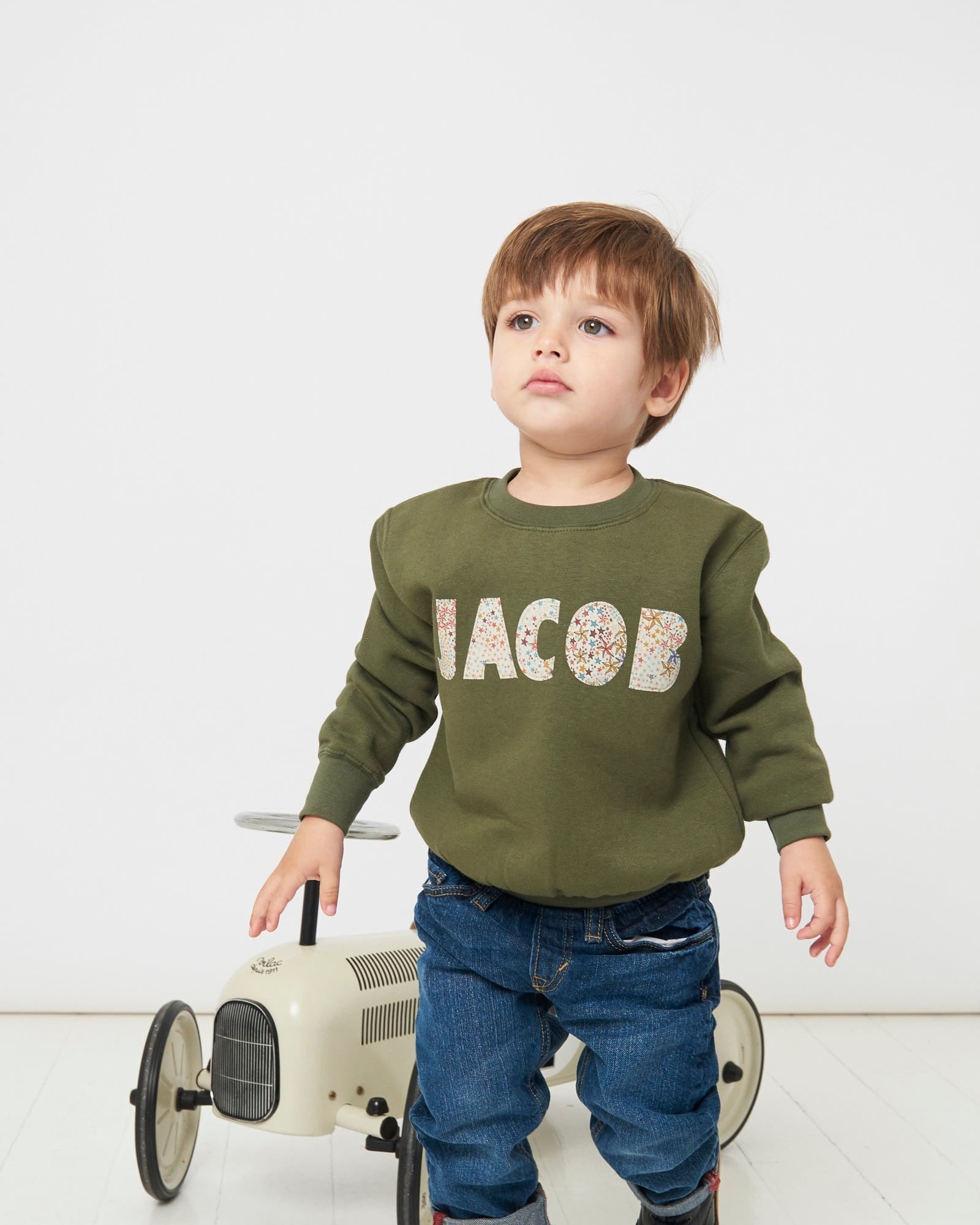 A 4 year old boy wearing a Magnificent Stanley khaki sweatshirt with his name 'Jacob' sewn on the front in a starry adelajda Liberty Print