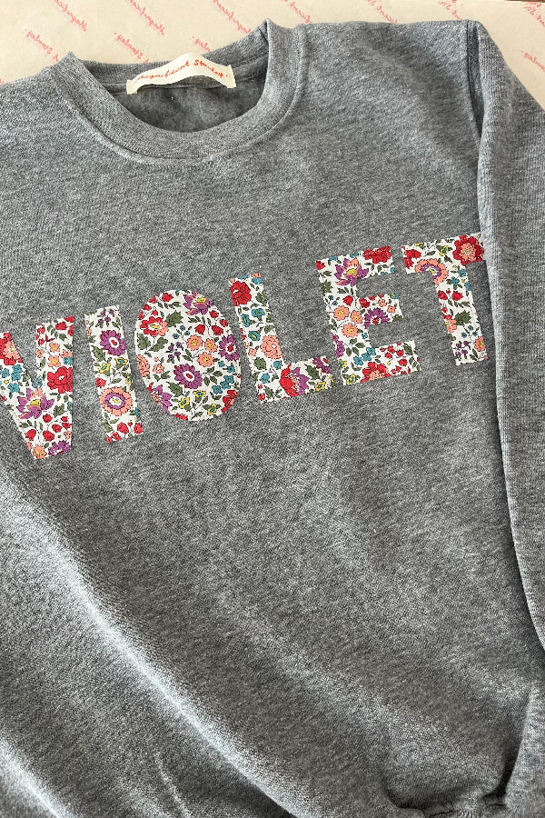 a grey sweatshirt with
a name in colourful letters in floral liberty print.