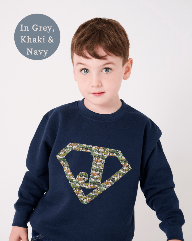 A 5 year old boy in a navy sweatshirt with his initial on the front in a superhero triangle cut from Liberty cars fabric.