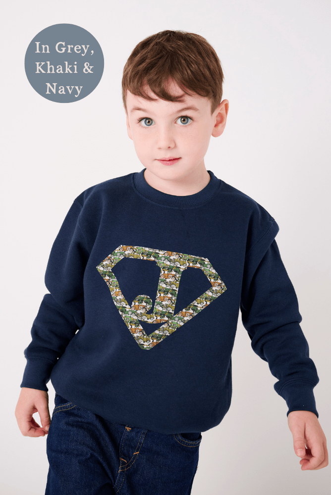 A 5 year old boy in a navy sweatshirt with his initial on the front in a superhero triangle cut from Liberty cars fabric.