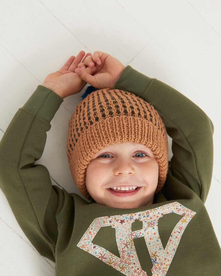 a happy kid in a Magnificent Stanley sweatshirt Superhero initial Khaki Sweatshirt in star Adelajda Liberty fabric
