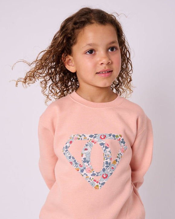 A young girl wearing a dusty pink sweatshirt with her initial sewn on the front in a Superhero motif made from floral Liberty Print.