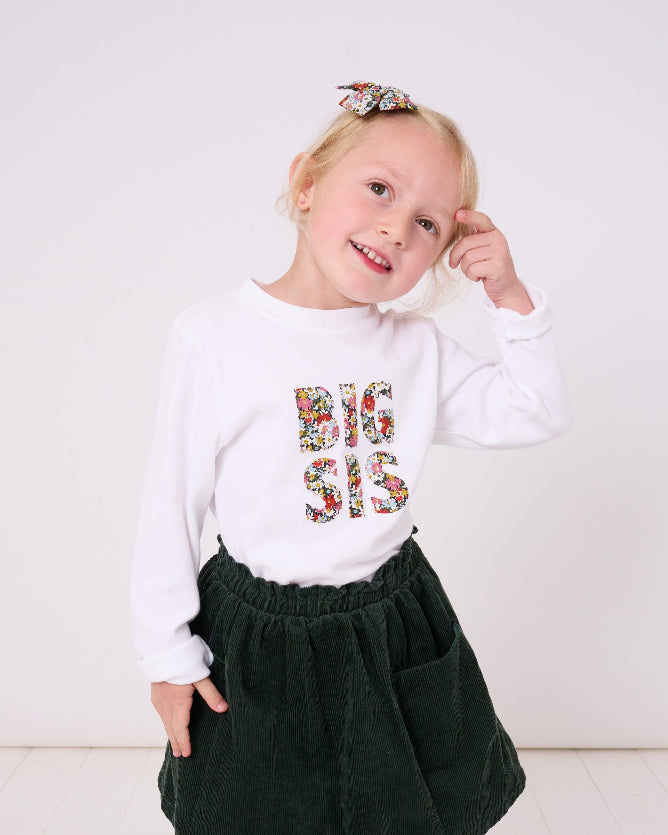5 year old girl who is a big sister wearing a white cotton t-shirt with BIG SIS in floral letters on the front. the letters are cut from Liberty print and appliquéd on.