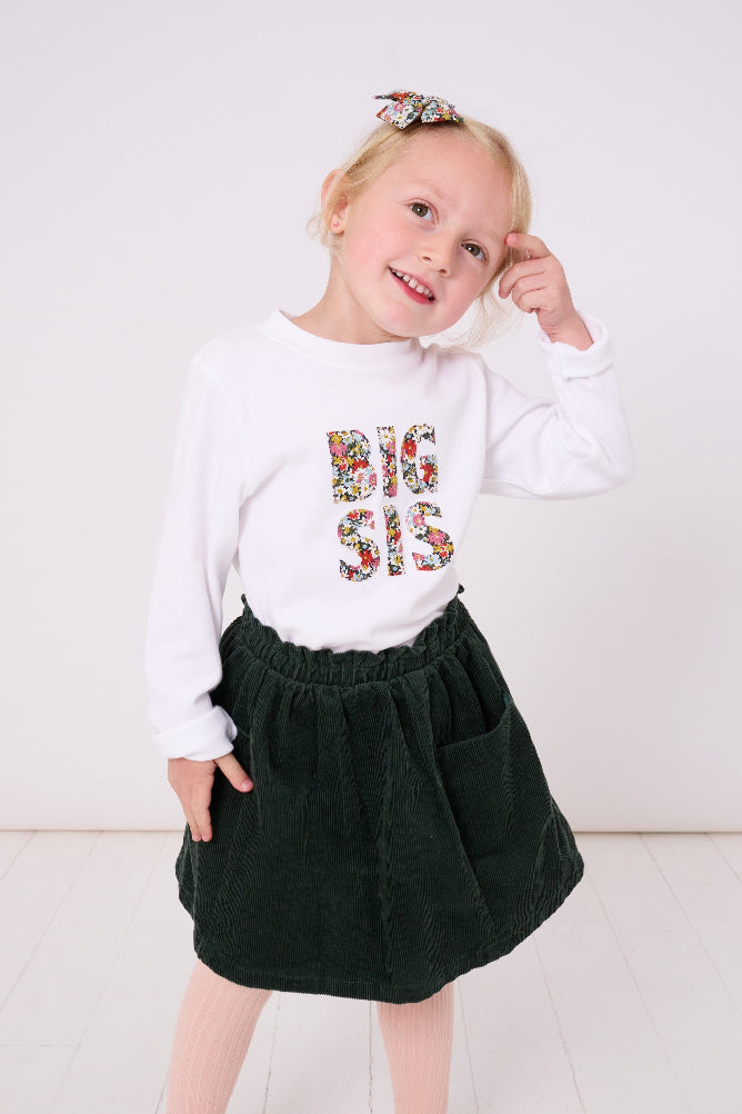 5 year old girl who is a big sister wearing a white cotton t-shirt with BIG SIS in floral letters on the front. the letters are cut from Liberty print and appliquéd on.