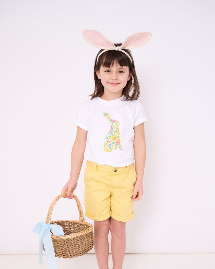 A smiling girl wearing a white cotton t-shirt with a floral liberty print bunny on the front and she has bunny ears on her head and carrying an Easter basket.