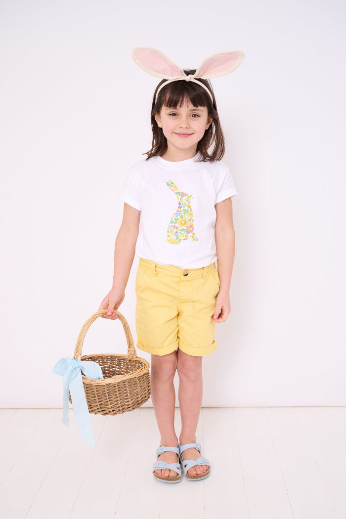 A smiling girl wearing a white cotton t-shirt with a floral liberty print bunny on the front and she has bunny ears on her head and carrying an Easter basket.
