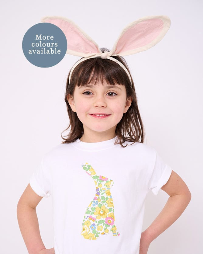 A smiling girl wearing a white cotton t-shirt with a floral liberty print bunny on the front and she has bunny ears on her head.