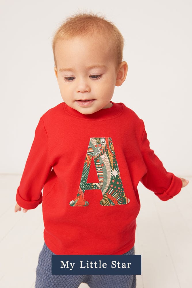 a 2 year old boy wearing a Magnificent Stanley long sleeve Red T-Shirt with his initial on the front in My Little Star Liberty Print