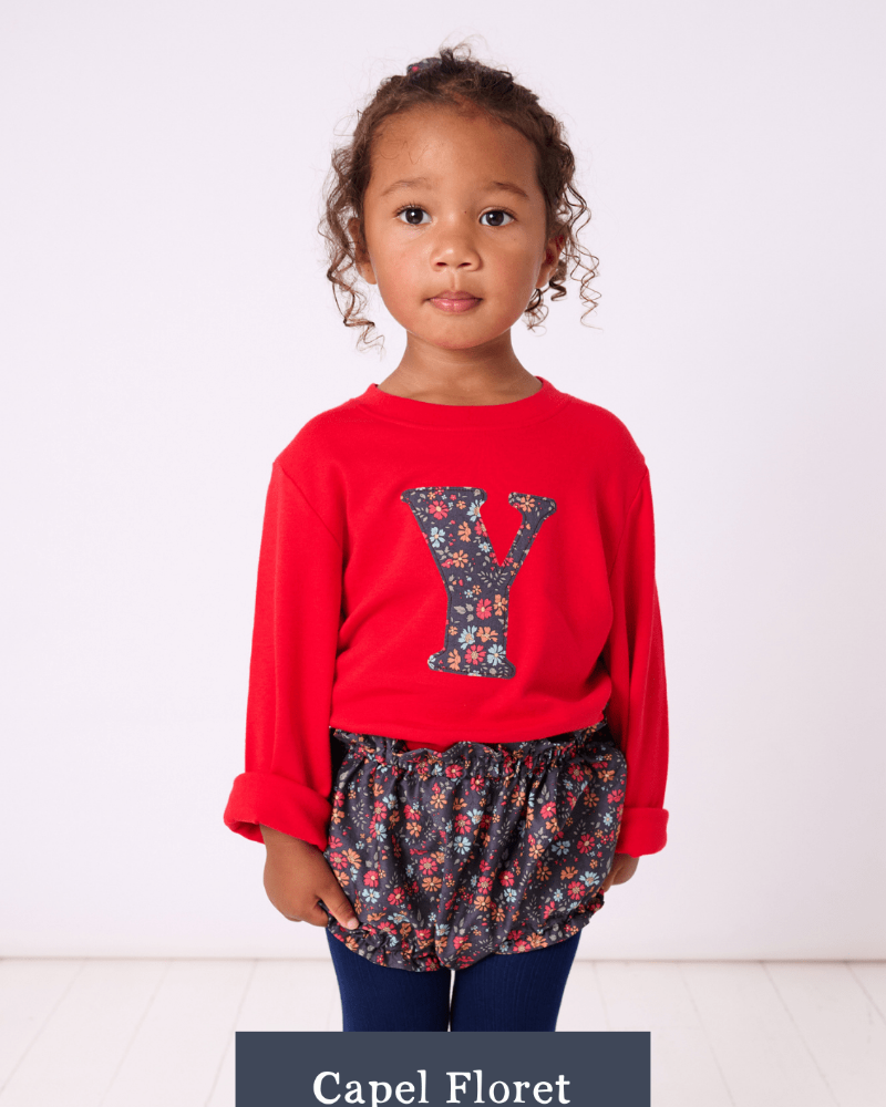 a 2 year old girl wearing a Magnificent Stanley long sleeve Red T-Shirt with her initial on the front in Capel Floret Liberty Print