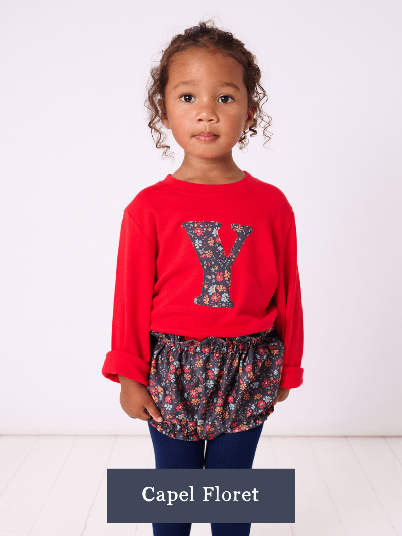 a 2 year old girl wearing a Magnificent Stanley long sleeve Red T-Shirt with her initial on the front in Capel Floret Liberty Print