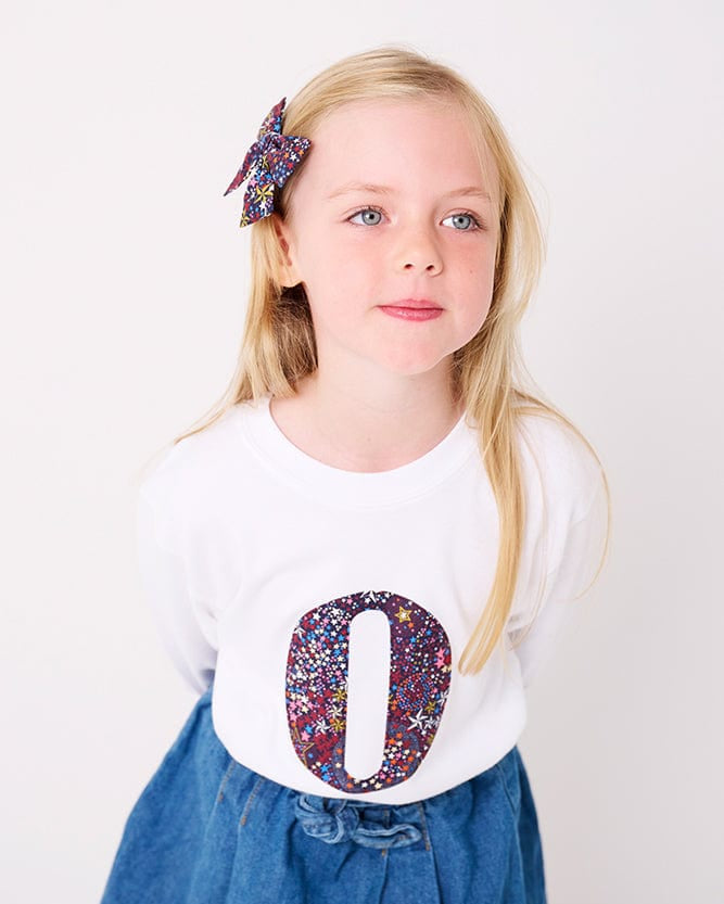 A 5 year old girl wearing a personalised white cotton t-shirt with her initial on in Adelajda's Wish Liberty fabric.