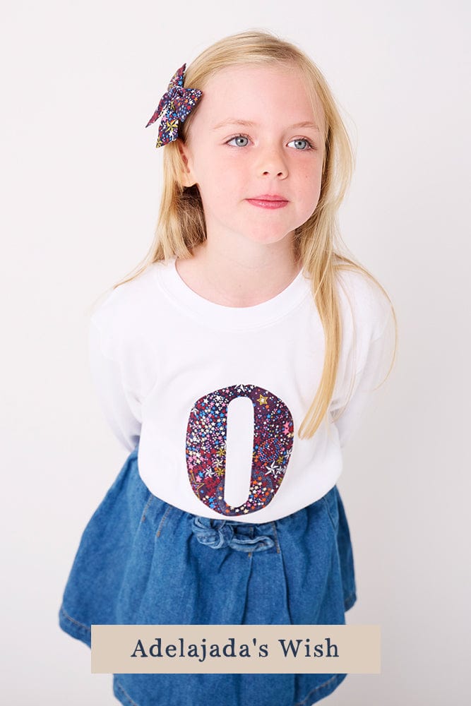 A 5 year old girl wearing a personalised white cotton t-shirt with her initial on in Adelajda's Wish Liberty fabric.
