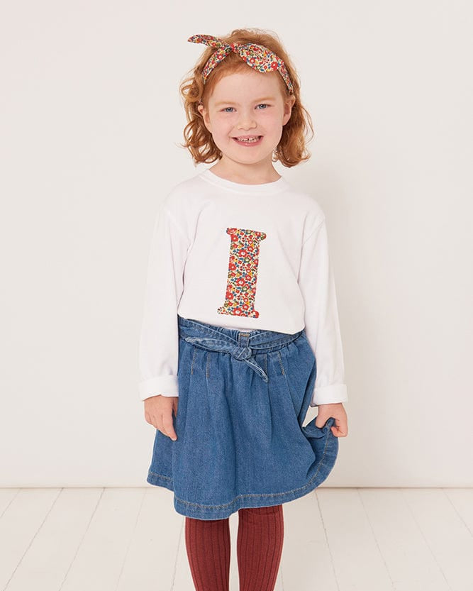 A 3 year old girl wearing a personalised white cotton t-shirt with her initial on in Betsy Ann floral Liberty fabric.