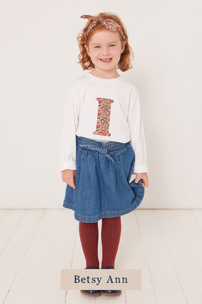 A 3 year old girl wearing a personalised white cotton t-shirt with her initial on in Betsy Ann floral Liberty fabric.