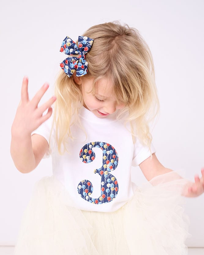 A 3 year old girl wearing a birthday white cotton t-shirt with a number 3 on in balloon Liberty fabric.