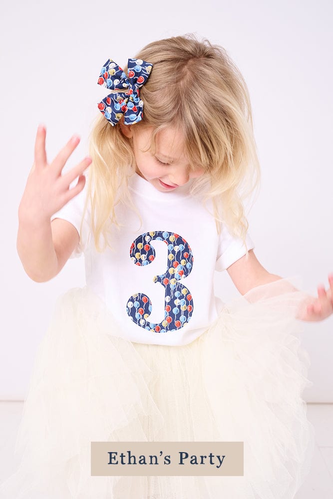 A 3 year old girl wearing a birthday white cotton t-shirt with a number 3 on in balloon Liberty fabric.