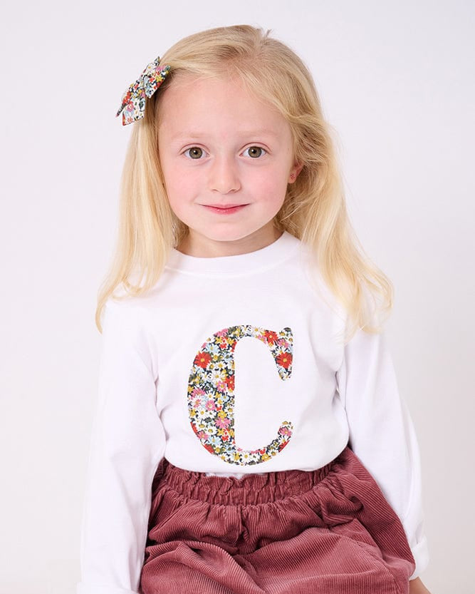 A 4 year old girl wearing a personalised white cotton t-shirt with her initial on in Libby floral Liberty fabric.