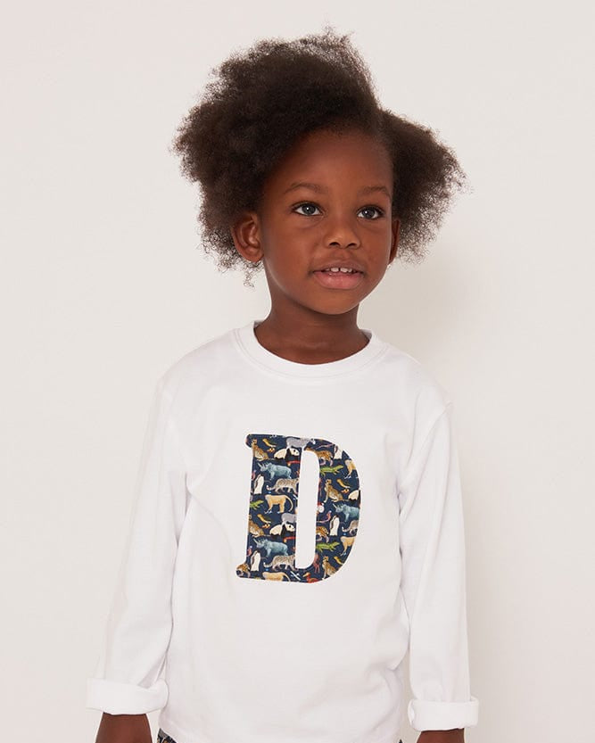 A 3 year old boy wearing a personalised white cotton t-shirt with his initial on in Quey zoo animal Liberty fabric.