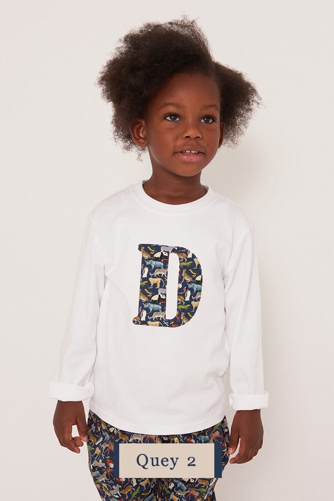 A 3 year old boy wearing a personalised white cotton t-shirt with his initial on in Quey zoo animal Liberty fabric.