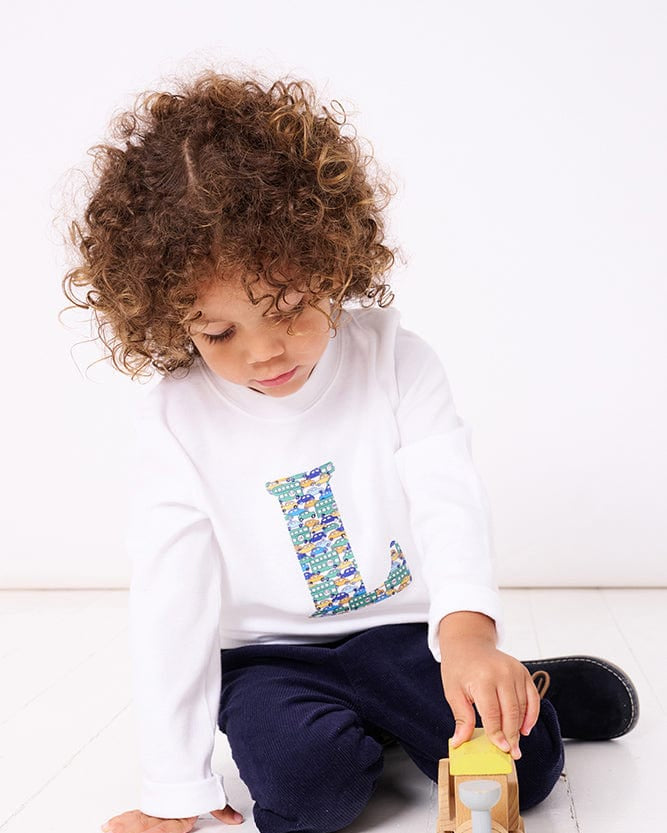 A 2 year old boy wearing a personalised white cotton t-shirt with his initial on in Hop On Hop Off Liberty fabric.