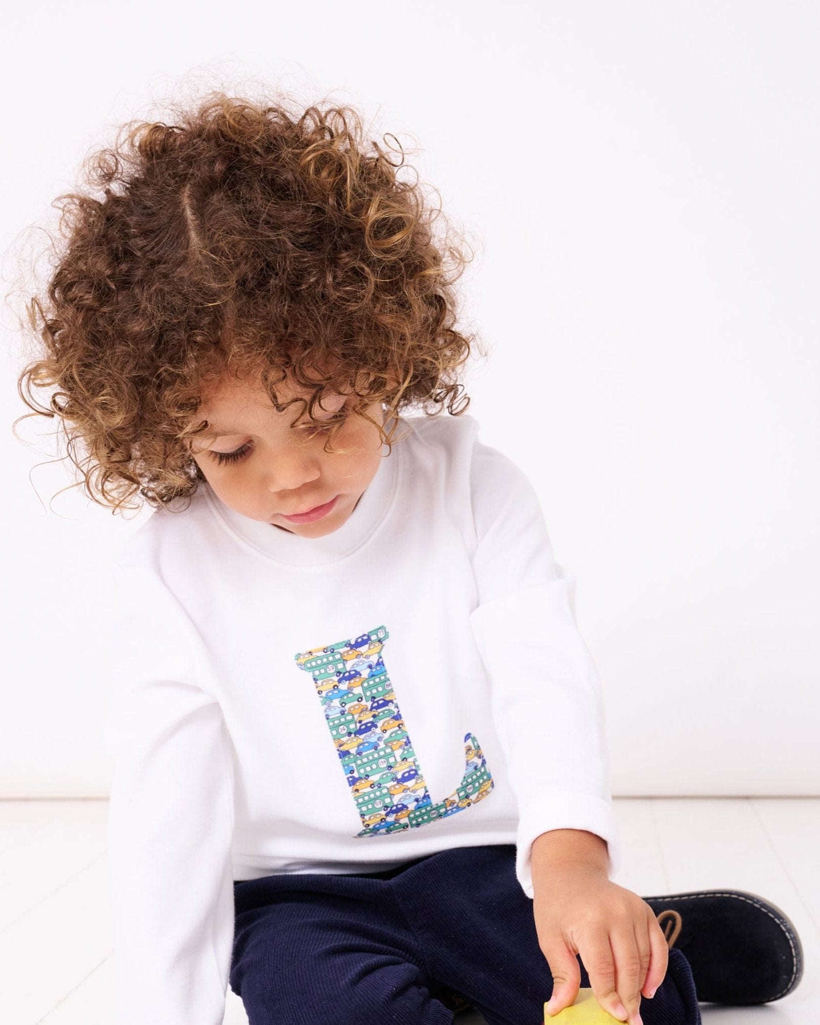 a 4 year old boy wearing a personalised kids white t-shirt with his initial cut from hop on hop off liberty cars print on the front