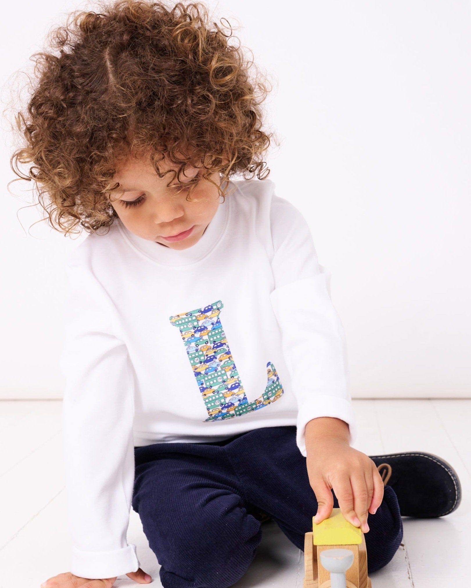 a 4 year old boy wearing a personalised kids white t-shirt with his initial cut from hop on hop off  liberty cars print on the front