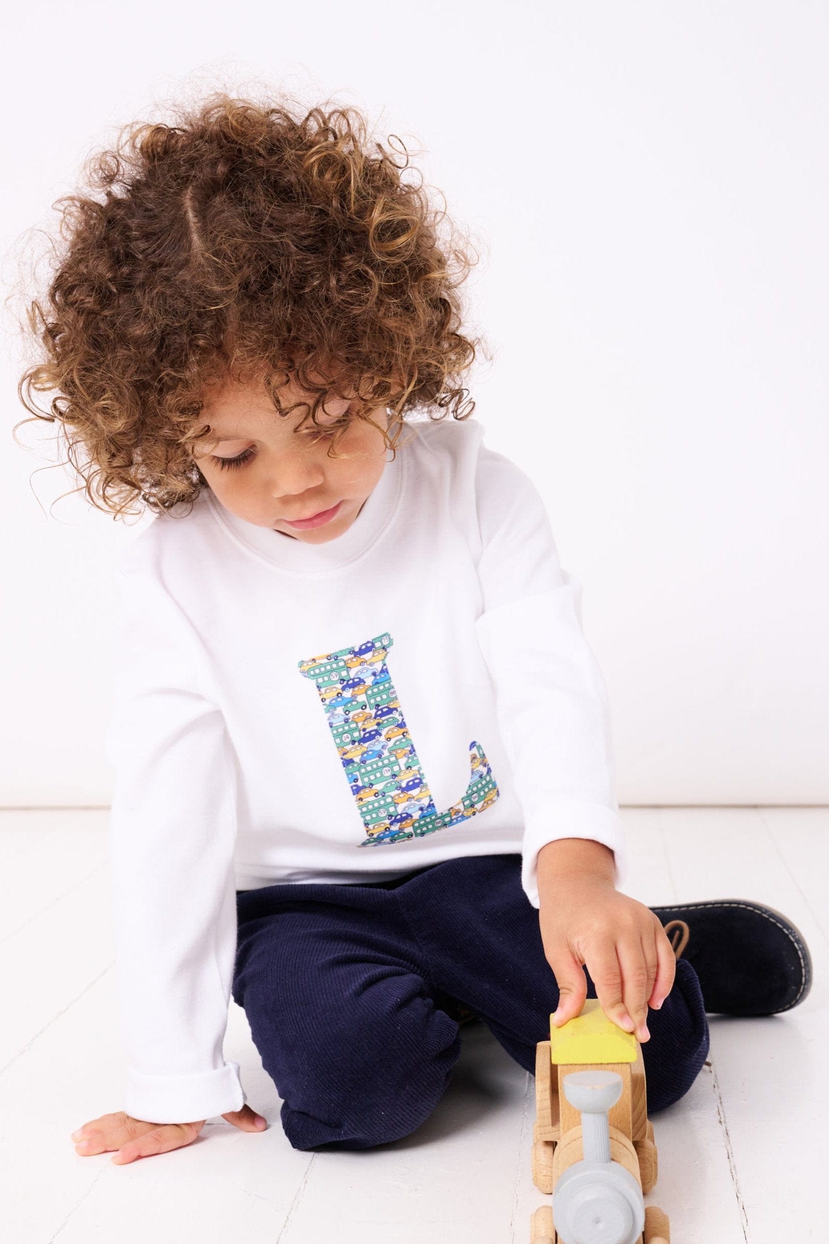 a 4 year old boy wearing a personalised kids white t-shirt with his initial cut from hop on hop off liberty cars print on the front