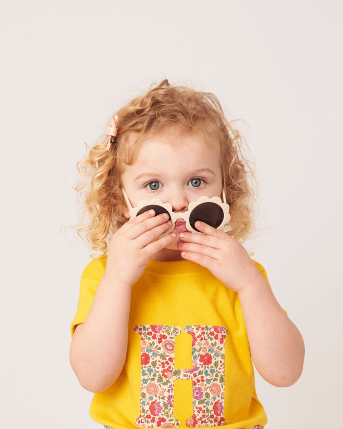 a smiling 2 year old girl wearing a personalised kids yellow t-shirt with an initial cut from d'anjo liberty floral print on the front