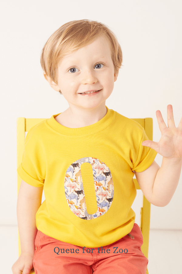 a smiling 3 year old boy wearing a personalised kids yellow t-shirt with an initial cut from queue for the zoo liberty animal print on the front