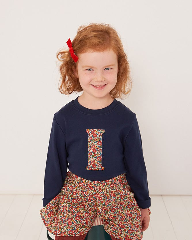 a 4 year old girl wearing a personalised kids navy t-shirt with an initial cut from betsy and liberty print on the front.