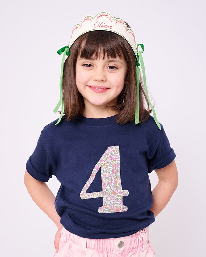 A smiling 4 year old girl wearing a birthday navy t-shirt with a liberty print number 4 on the front.