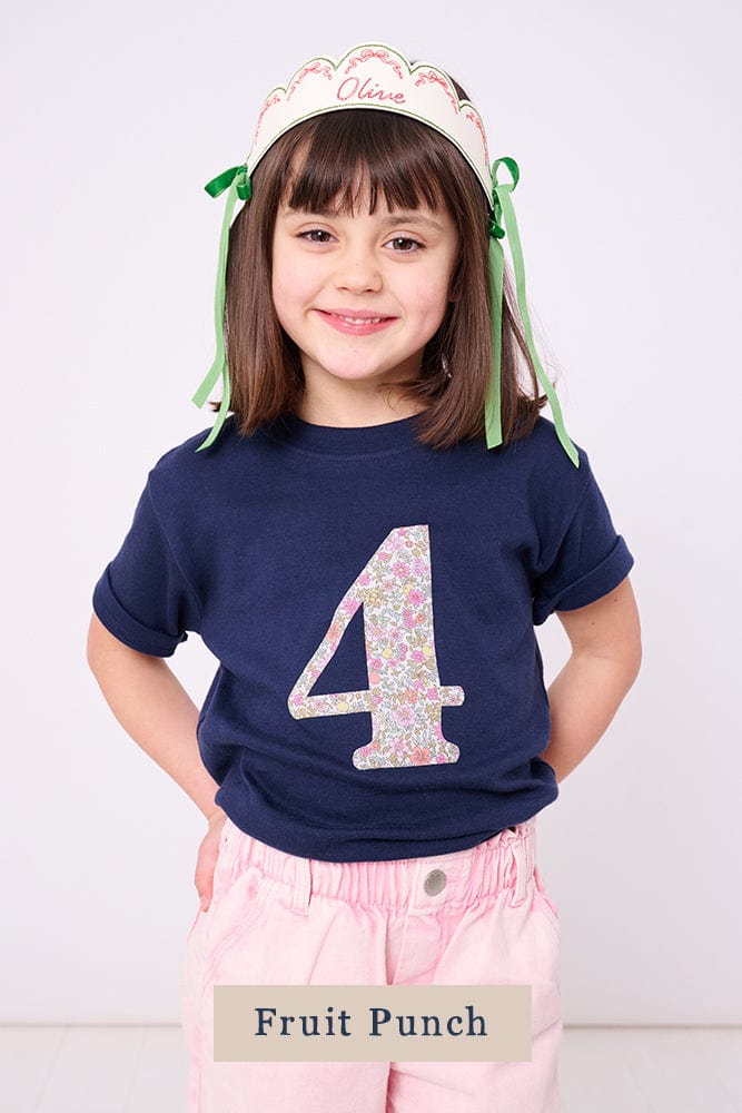A smiling 4 year old girl wearing a birthday navy t-shirt with a liberty print number 4 on the front.