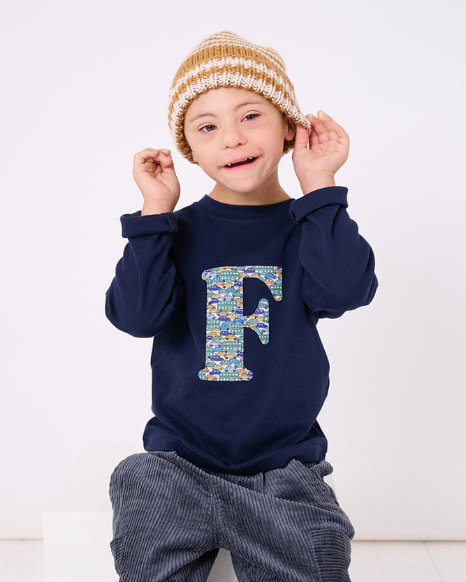a 4 year old boy wearing a personalised kids navy t-shirt with an initial cut from hop on hop off liberty cars print on the front