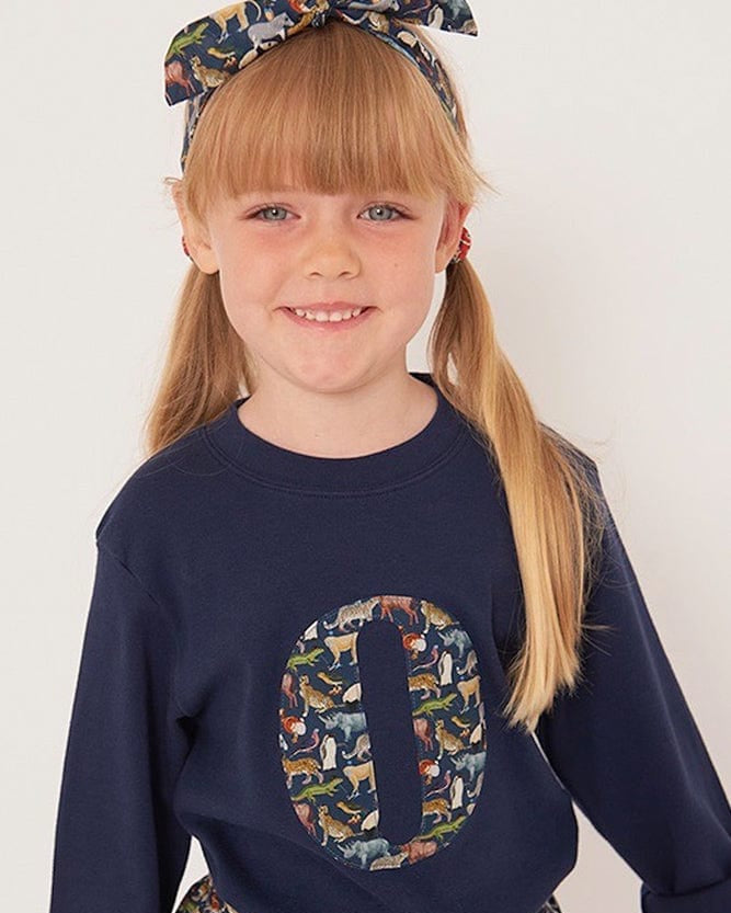 a 5 year old girl wearing a personalised kids navy t-shirt with an initial cut from Quey 2 liberty zoo animal print on the front