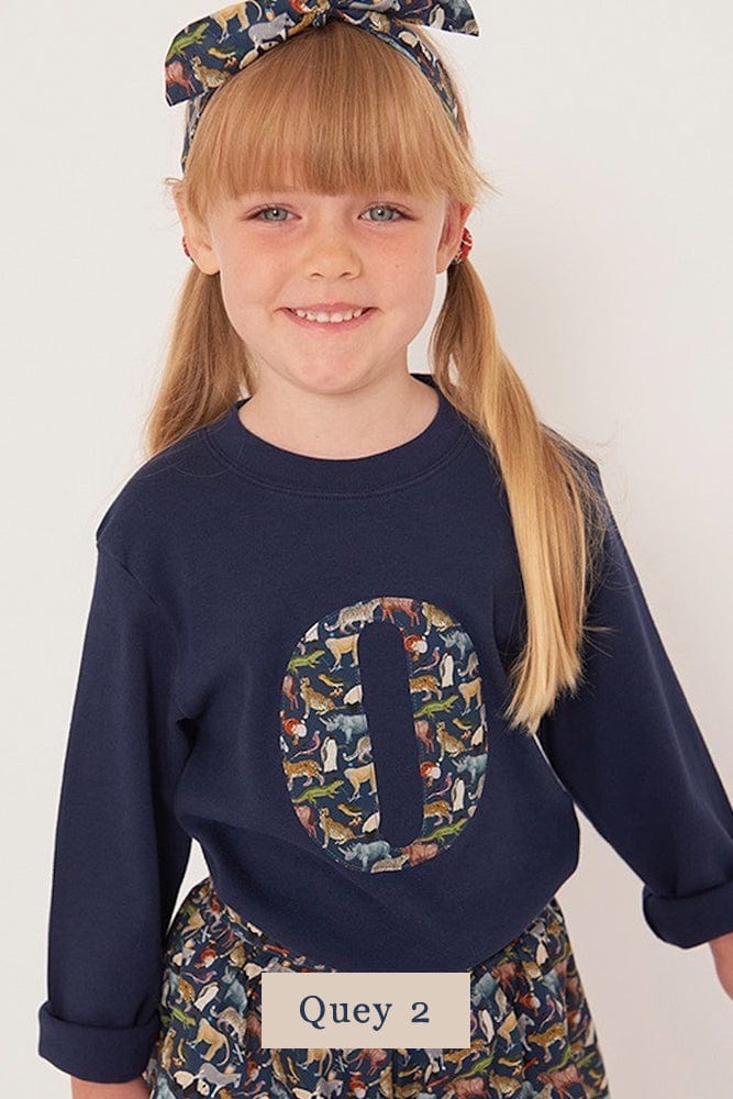 a 5 year old girl wearing a personalised kids navy t-shirt with an initial cut from Quey 2 liberty zoo animal print on the front
